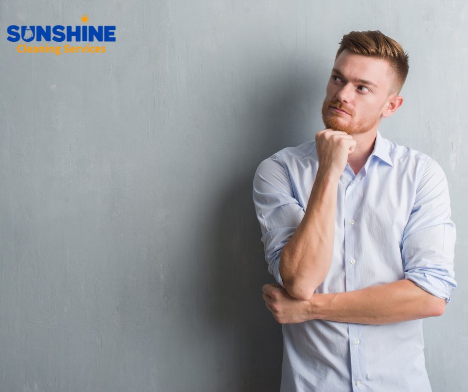 A contemplative man wearing a light blue shirt stands against a gray wall with a "Sunshine Cleaning Services" logo in the top-left corner of the image.